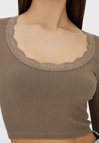 Bruin, geribd, langermig shirt met een brede, ronde halslijn en een fijn bewerkte beige kanten rand, die textuur en gedetailleerd ontwerp benadrukt.