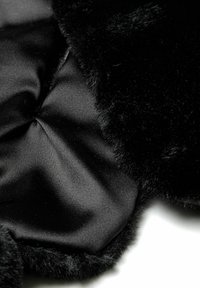Tissu en fausse fourrure noire et en satin, présentant une surface lisse et brillante ainsi qu'une texture douce et pelucheuse avec des bords arrondis et un détail central froncé.