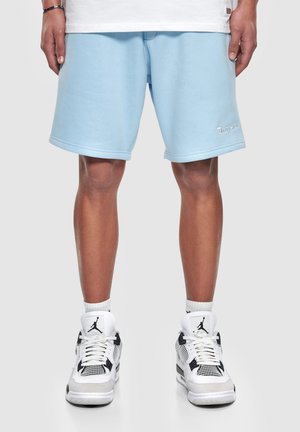 Shorts bleu clair en mélange coton avec une taille élastique et un logo brodé ; associés à des baskets blanches avec des accents noirs.
