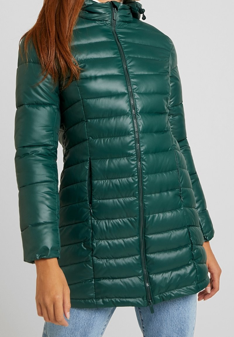 Chaqueta de plumas verde acolchada con cuello alto y cierre de cremallera. Presenta costuras horizontales y puños elásticos. Textura suave y brillante.