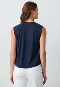 Top senza maniche di colore blu navy con scollatura rotonda, realizzato in tessuto liscio, caratterizzato da una vestibilità comoda e orlo curvo, abbinato a jeans bianchi.