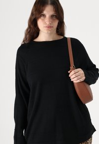 Black long-sleeve sweater with subtle horizontal stripes, made of a soft fabric. A brown crossbody bag is held by the person wearing it.