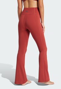 Pants de yoga rouges évasés en tissu extensible. Dotés d'une taille haute, de coutures orange et d'un petit logo au dos.