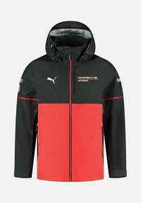 Czarna i czerwona kurtka z zamkiem z przodu, kapturem i akcentami z logo. Posiada design w kolorowe bloki, teksturę materiału i sportowy styl.