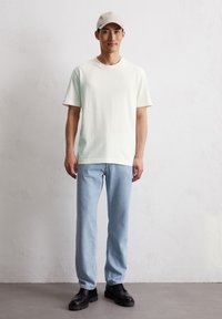 T-shirt en coton vert clair avec des manches courtes, associé à un jean en denim bleu clair. Des chaussures noires à lacets complètent le look décontracté.