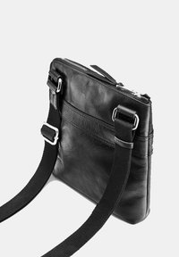Černá kožená crossbody taška se zipovým uzávěrem, nastavitelným textilním popruhem a hladkým povrchem. Má přední kapsu a stříbrné kovové detaily.