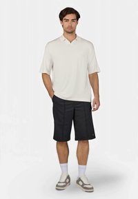 Light-colored polo shirt with short sleeves, paired with black knee-length shorts. Model wears white crew socks and light sneakers.