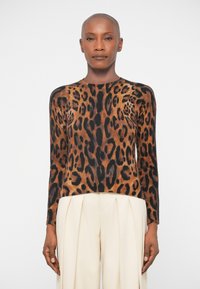 Leopardmönstrad tröja i nyanser av brunt och svart. Ribbad textur, långa ärmar, rundad halsringning. Matchad med ljusa, plisserade byxor.