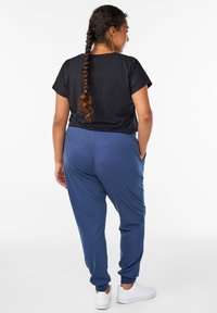 Black short-sleeve top paired with navy blue sweatpants, featuring elastic cuffs, side pockets, and white sneakers. Smooth fabric texture.