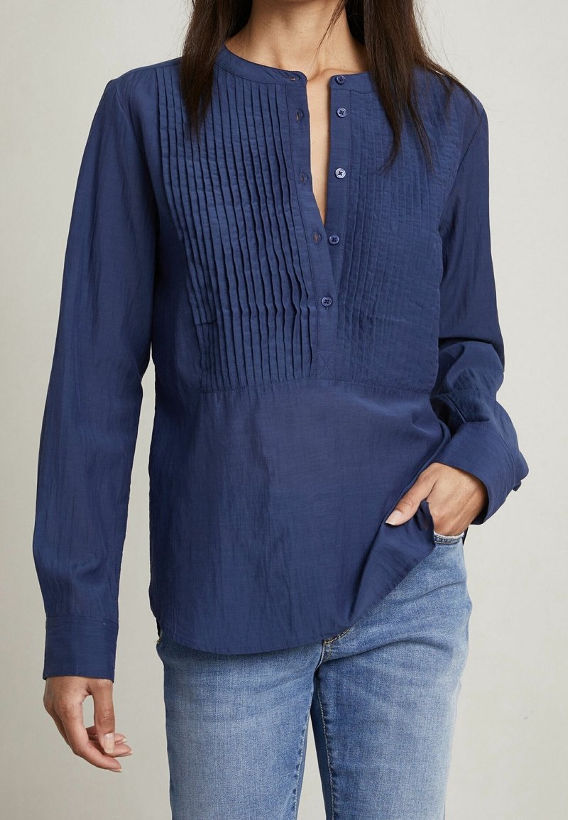 Camicia a maniche lunghe blu navy con chiusura a bottoni e dettagli plissettati sul davanti, realizzata in un tessuto leggero e testurizzato.