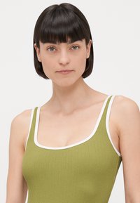 Débardeur vert à côtes avec bord blanc, présentant un décolleté arrondi et des fines bretelles, fabriqué dans un tissu texturé.