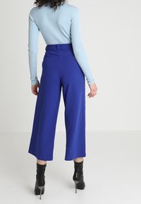 Haut à manches longues bleu côtelé rentré dans un pantalon large à taille haute bleu royal. L'ensemble est complété par des bottines noires à talons.