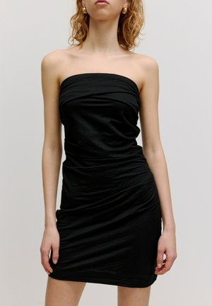 Zwarte strapless jurk van kreukelig materiaal. Aansluitend ontwerp met geplooide details bij de taille, tot halverwege de dij. Glad textuur.