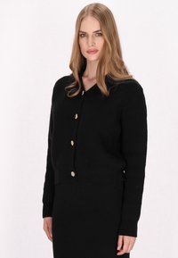 Schwarze Strickjacke mit V-Ausschnitt, cropped Design, mit goldfarbenen Knöpfen und gerippten Bündchen. Glatte Textur mit taillierter Silhouette.