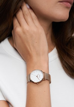 Montre ronde avec un cadran blanc et des accents en or rose, dotée d'un bracelet en maille. Le design est élégant et minimaliste, adapté à un poignet mince.
