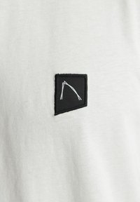 Witte t-shirt met een zwart rechthoekig label en een witte grafisch ontwerp. De stof lijkt zacht en lichtgewicht te zijn.