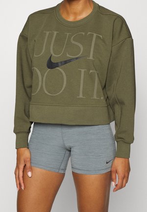 Personne portant un sweat-shirt Nike vert olive avec le texte "Just Do It" et un logo swoosh noir, et un short de sport Nike gris clair avec logo swoosh noir.