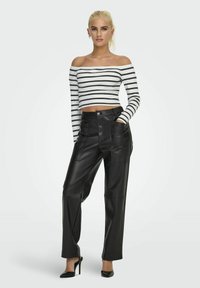 Crop top w paski, z odsłoniętymi ramionami w białym i czarnym kolorze, z długimi rękawami, połączony z czarnymi spodniami skórzanymi z wysokim stanem i kieszeniami.