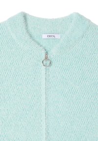 Cardigan en tricot bleu clair avec fermeture éclair, présentant un motif texturé et une apparence douce et duveteuse. L'étiquette indique "CECI".