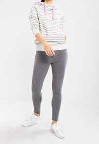 Sudadera a rayas gris claro con detalles en rosa, bolsillo tipo canguro y pantalones vaqueros ajustados grises. Zapatillas blancas completan el conjunto casual.