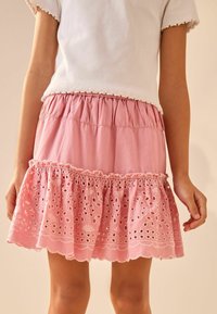 Jupe en coton rose avec un ourlet à volants, ornée d'une broderie délicate en œillets et d'une taille froncée. Associée à un dessus blanc côtelé.