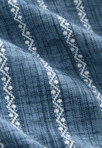 Tissu bleu à tissage texturé, présentant des motifs en zigzag blancs. La surface est légèrement texturée, créant une profondeur visuelle.