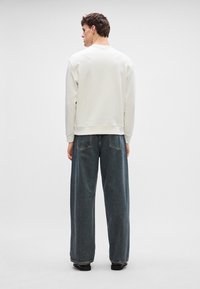 Krémová mikina se žebrovanými manžetami a lemem, spárovaná s volnými tmavě modrými džíny z denimu se kontrastním prošíváním a kapsami.