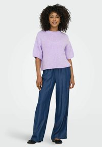 Lavenza adīta džemperis ar īsām, nedaudz pūkām piedurknēm, kombinēts ar platām, tumšām džinsa biksēm un melniem plakaniem zābakiem.