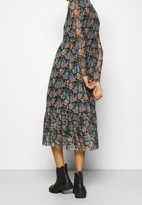 Transparent, blomsterprintet midi-kjole med lange ærmer, flæsekant og mørk bundfarve. Kombineret med sorte ankelstøvler, der viser stilfulde designdetaljer.