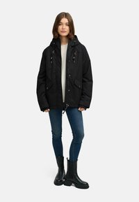 Svart isolerad parkas med huva, två framfickor och snörningsdetaljer. Matcher med blå smala jeans och svarta ankelboots.