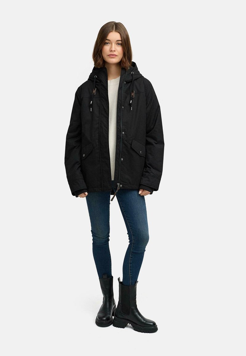 Svart isolerad parkas med huva, två framfickor och snörningsdetaljer. Matcher med blå smala jeans och svarta ankelboots.