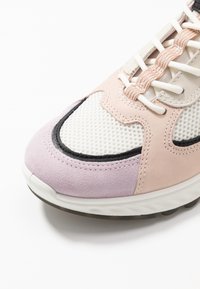 Sneaker caratterizzata da un mix di suede rosa chiaro e materiali in rete, dettagli neri e una suola bianca arrotondata con battistrada testurizzato.