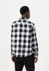 Zwart-wit geruite button-up shirt, lange mouwen, gemaakt van geweven stof, met contrasterende patronen en een gebogen zoom.