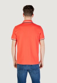 Polo rosso con un colore uniforme, maniche corte e colletto bicolore con righe navy e bianche, abbinato a jeans blu.