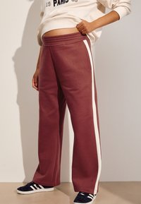 Mørkerøde joggingbukser med hvide sidelister, der har en afslappet pasform og elastisk talje. Blødt stof med lommer i siderne.