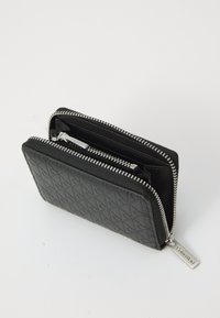 Black zippered wallet with embossed pattern and silver Calvin Klein zipper pulls, shown partially open on white background.