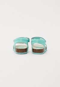 Turkise sandaler med åpen bak, justerbar stropp og teksturert korksåle. Den hvite innermaterialet har et lyst mønster.