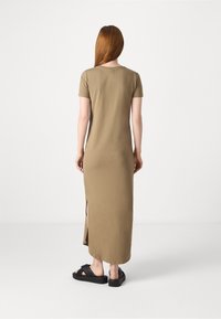 Robe maxi kaki à manches courtes, fentes latérales et coupe décontractée. Le mannequin porte des sandales à plateforme noires sur un fond uni.