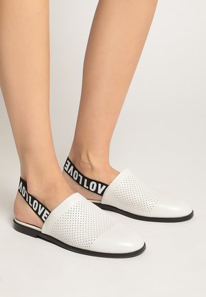 Scarpe bianche senza lacci con design perforato, fascia elastica nera con la scritta "LOVE", suola piatta e texture liscia.