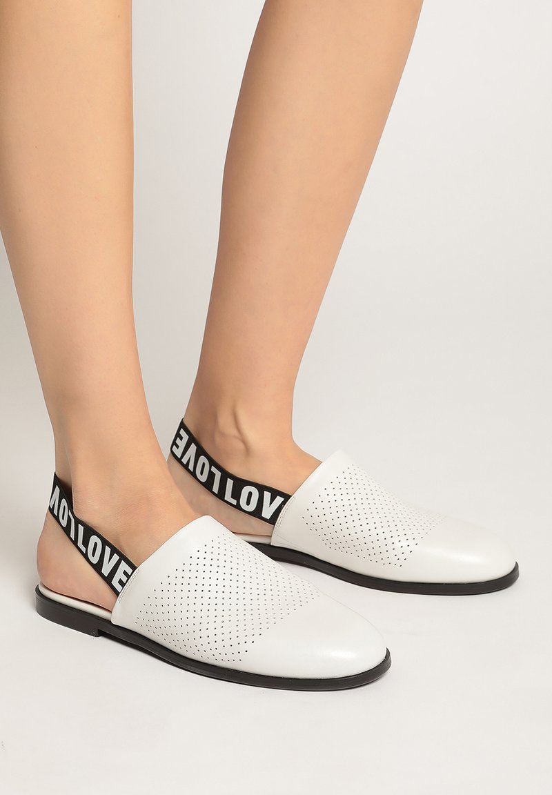 Zapatos blancos tipo slip-on con diseño perforado, banda elástica negra que muestra la palabra "AMOR", suela plana y textura suave.