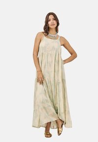Vestido maxi en beige claro con patrones en acuarela verde pastel. Cuenta con un diseño sin mangas, cintura fruncida y una falda con capas.
