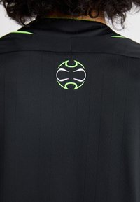 Sort skjorte med lodrette striber, der har et cirkulært logo i hvid og neon grøn på ryggen. Glat tekstur, afdæmpet design, kort krave.