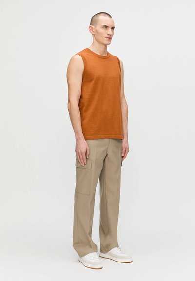 Haut sans manches en tricot couleur rouille associé à un pantalon cargo beige clair avec poches latérales, porté avec des baskets blanches.
