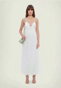 Bela, dolga obleka z globokim V-izrezom in tankimi naramnicami, ki ima teksturno mrežasto vzorčenje. V kombinaciji z svetlo zeleno torbico.