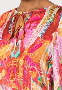 Bunte Bluse mit einer Mischung aus pinken, roten und orangefarbenen abstrakten Mustern, weichem Stoff, Schlüssel- oder Ausschnitt mit gebundenem Detail und strukturiertem Finish.