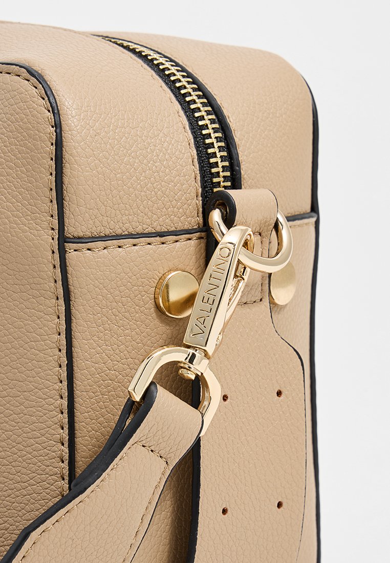 Beige Lederhandtasche mit strukturiertem Finish, schwarzen Akzenten, hardware in goldfarbener Ausführung und einem Reißverschluss mit einem gebrandeten Verschluss sowie einem verstellbaren Trageriemen.