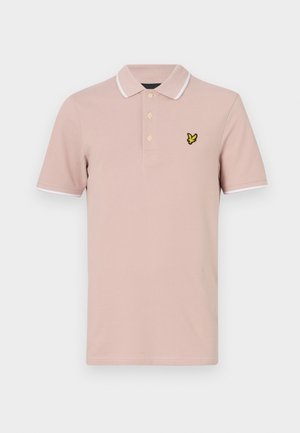 Polo rose clair avec une patte de boutonnage à trois boutons, bord blanc sur le col et les manches, avec un logo brodé jaune sur la poitrine.