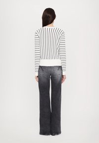 Pull rayé blanc et noir avec un ourlet côtelé, associé à un jean denim gris à jambes larges présentant une texture délavée et des poches arrière.