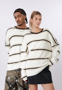 Ριγέ, φαρδιά πλεκτά τοπ σε λευκό με καφέ οριζόντιες γραμμές. Υφασμάτινη υφή, λαιμός κοτλέ, φαρδιά μανίκια. Συνδυασμένα με παντελόνια με σχέδια και δερμάτινα.