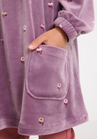 Lila Samtkleidungsstück mit einer Fronttasche, die florale Musterdetails aufweist, und elastischen Bündchen. Weiche Textur, legeres Design.